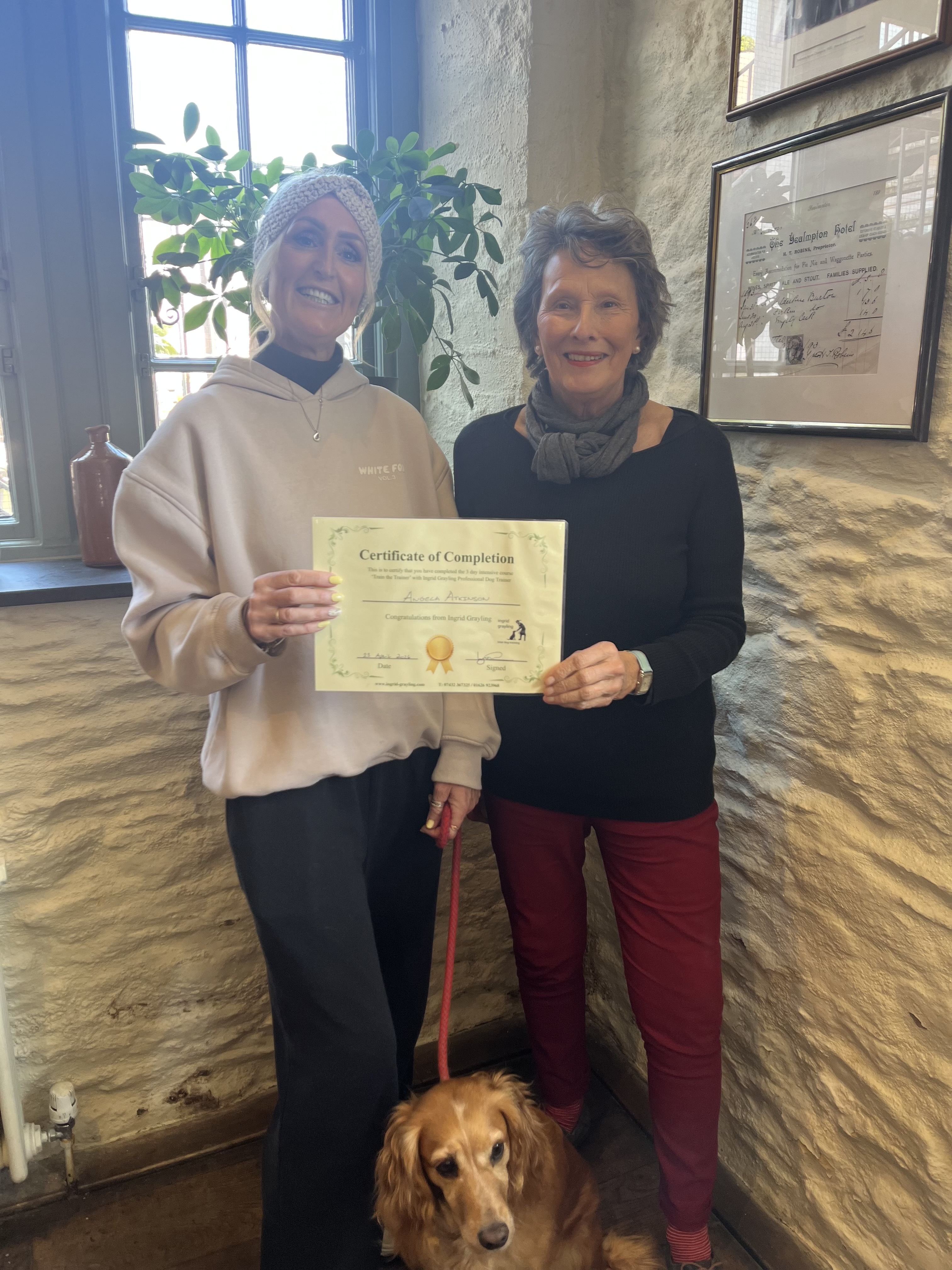 Angela Atkinson with her mentor Ingrid Grayling and a Cocker Spaniel, holding her Certificate of Completion